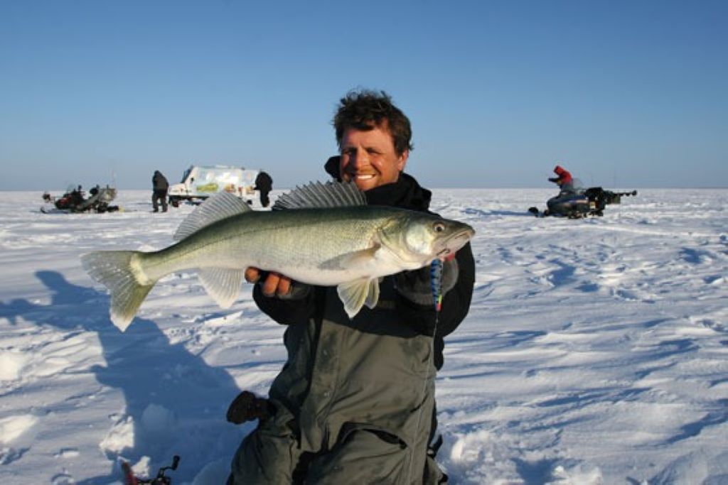 Angler holding a shiny ice fishing spoon over a hole in the ice in Canada during winter
