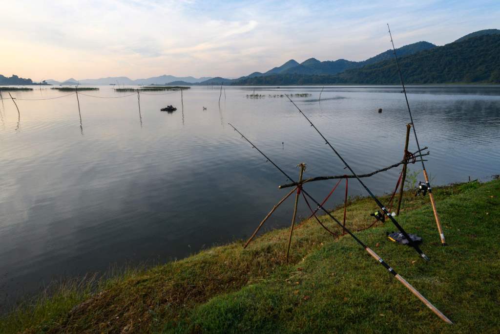 Angler casting fishing rod on calm lake at sunrise