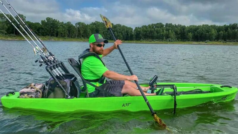 Angler fishing from stable kayak on calm lake at sunrise