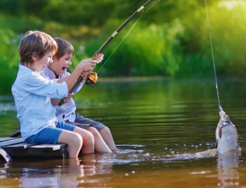 Colorful beginner fishing rod designed for kids placed on grass near a small tackle box