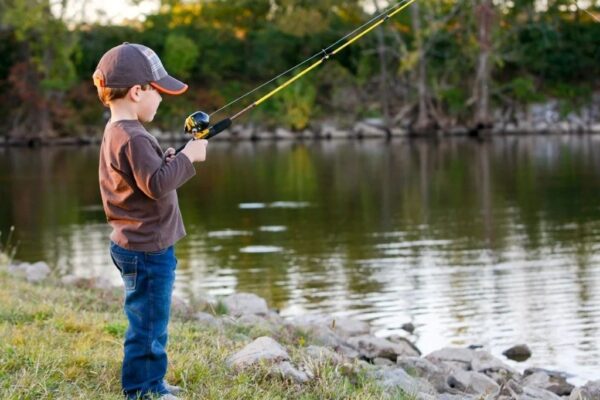 Child holding a lightweight kids fishing rod while fishing by a calm lake with adult supervision